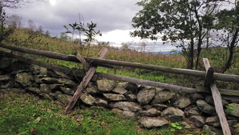 a rustic wood fence over a dry stacked stone wall beside a field