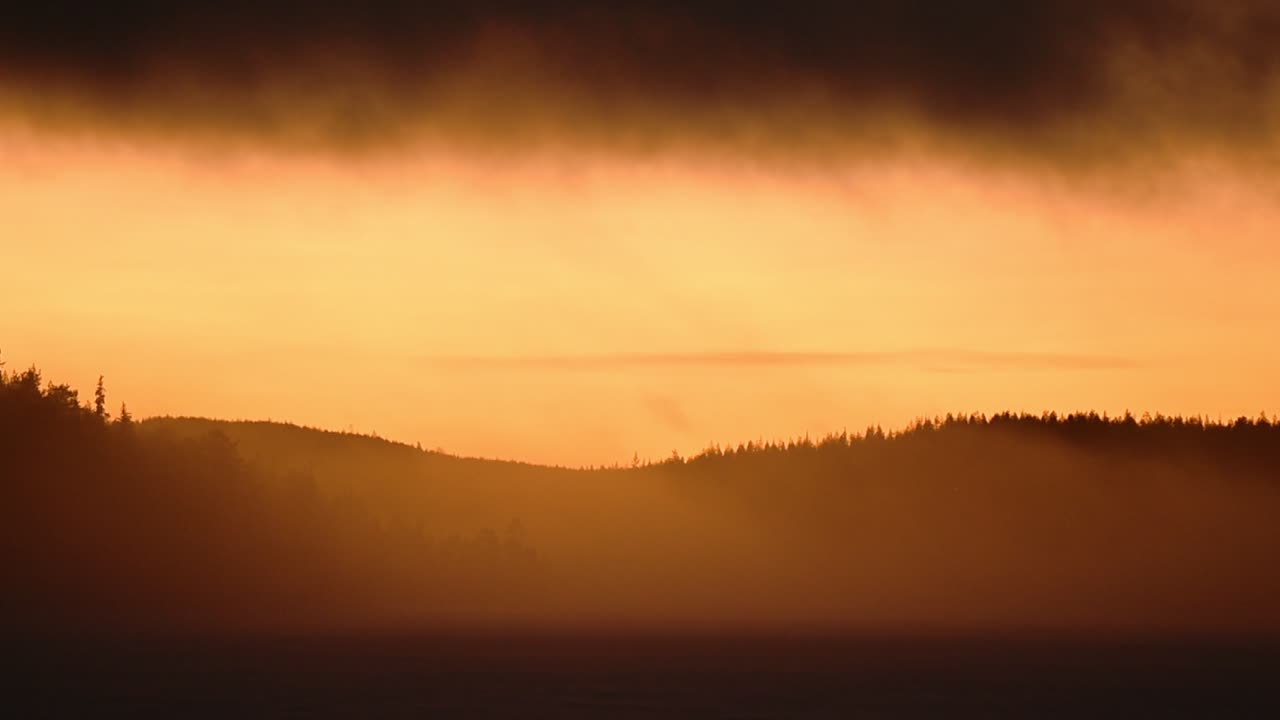 Landscape view of a bright orange sunrise over a frozen lake, on a misty morning, in Lapland, Finland