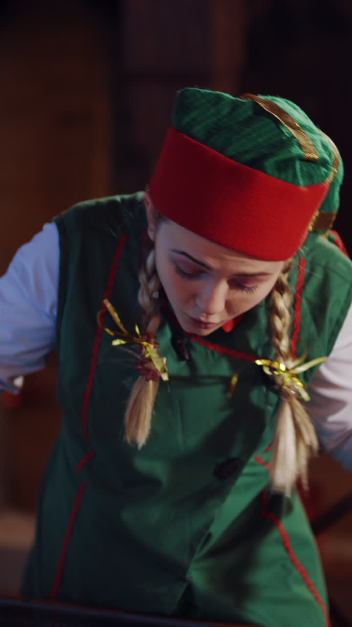 Funny elf holding stack of envelopes for Santa. Dispersed young elf with letters. Envelopes falling on the table from girl's hands on the Christmas tree background. Vertical video