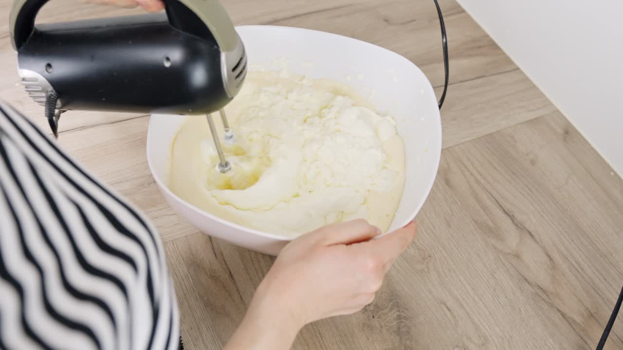 Whipping cream with a hand mixer, close-up shot of a bowl on a wooden surface