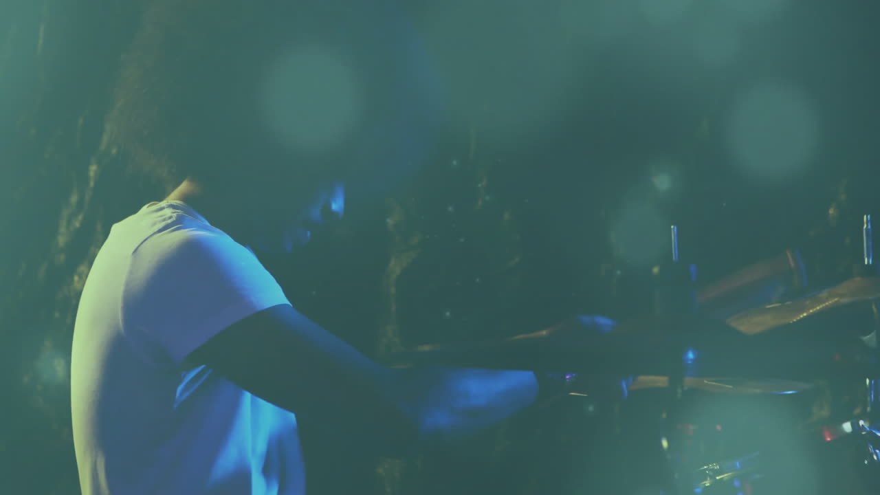 Batterista che tiene le bacchette sul palco, fondendo la performance dal vivo con sovrapposizioni animate di onde sonore.