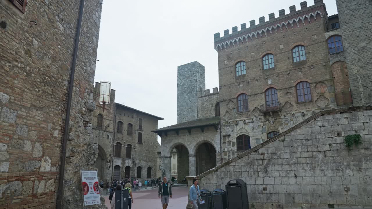 Piazza del Duomo con persone che passeggiano di giorno a San Gimignano, Italia.