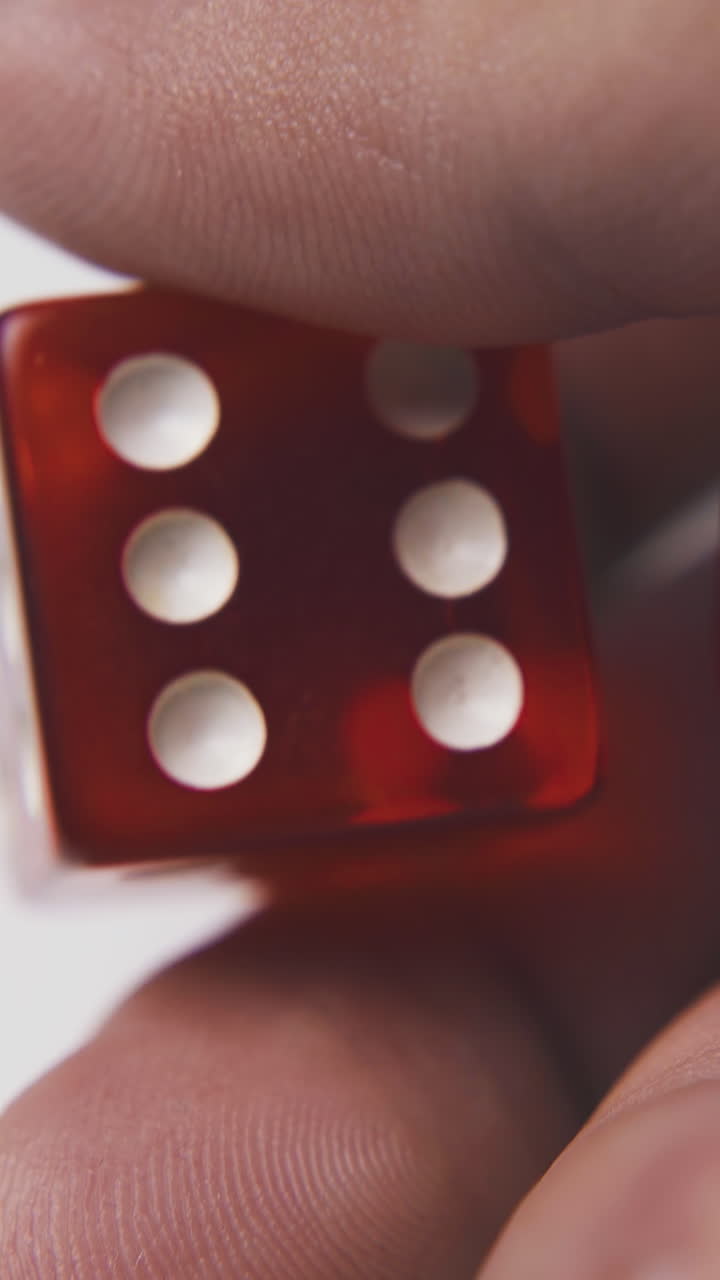 young man holds red plastic dices with white spots on palm in light background extreme close view