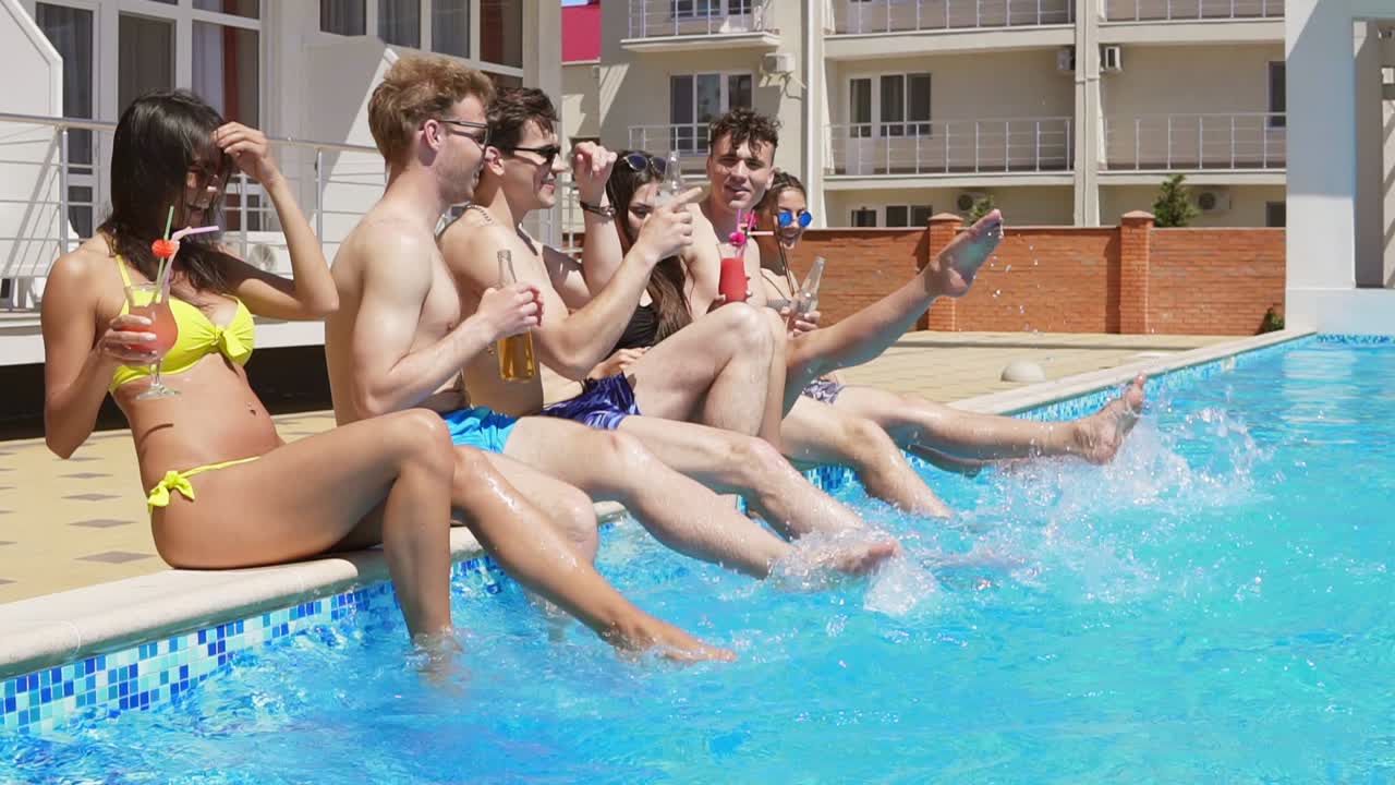 夏のプール パーティーを楽しんでいる友人の幸せなグループは水しぶきと水の中で自分の足を蹴る