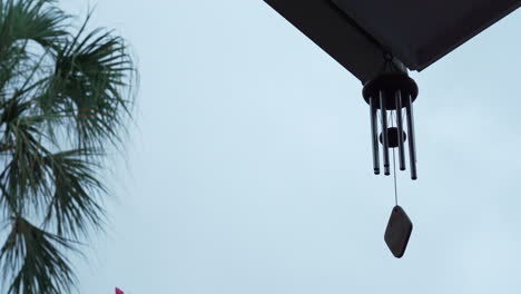 Calming-and-relaxing-view-of-a-wind-chime-blowing-in-a-tropical-garden-while-it's-raining