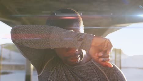 animation of glowing lights over running african american man taking a break, wiping brow in the sun