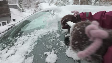 person scraping ice off car windshield in winter using scraper