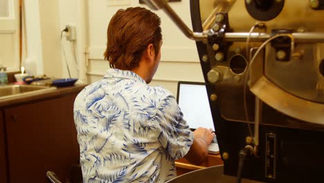 man using laptop while sitting besides coffee roasting machine