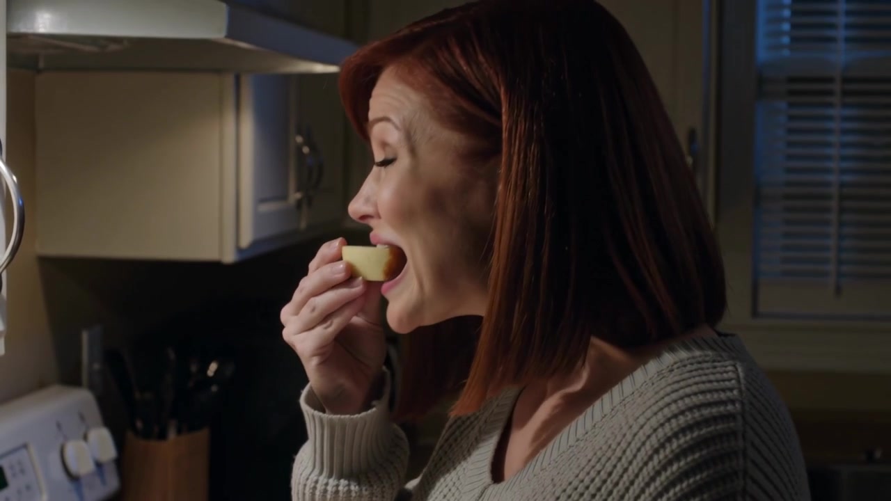 Woman in gray top seeing sauce dripping in kitchen, raising sauced apple, tasting, copy space