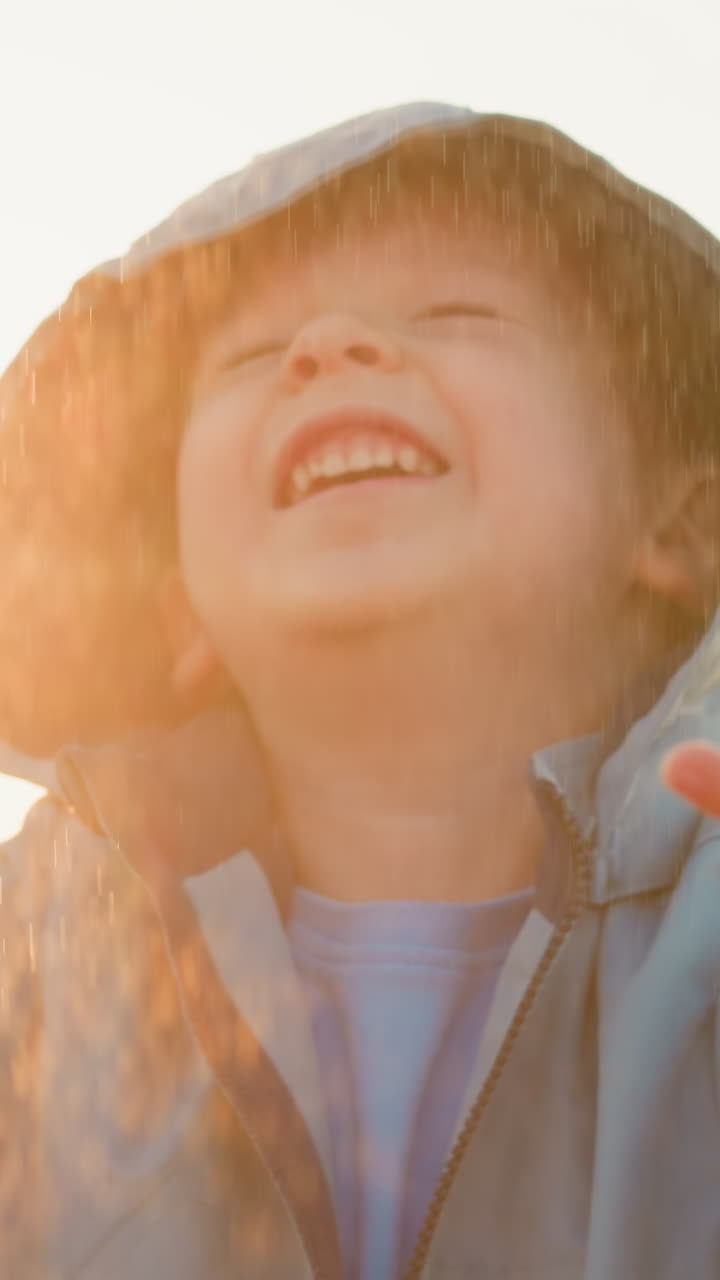 Boy holds out palms feeling warm rain. Lively toddler adorned in bright raincoat frolics in pouring rain reveling in countryside charm. Happy childhood