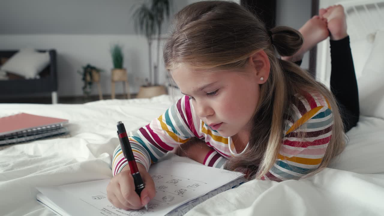 Elementary age girl studying while lying on front on the bed