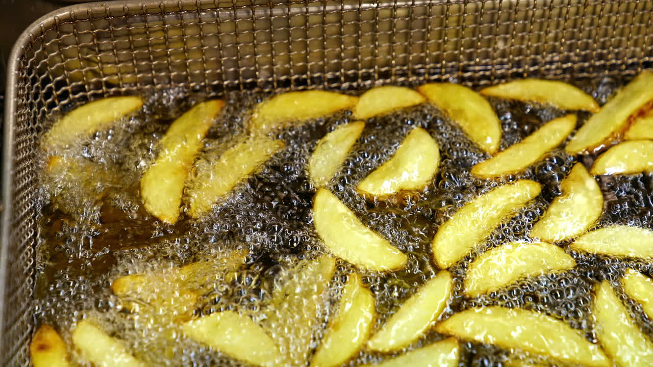 Fries fried in oil at restaurant. Close up of potatoes frying on hot boiling oil