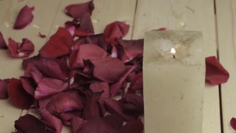 Red-rose-flower-petals-falling-onto-wooden-floor-with-lit-candle