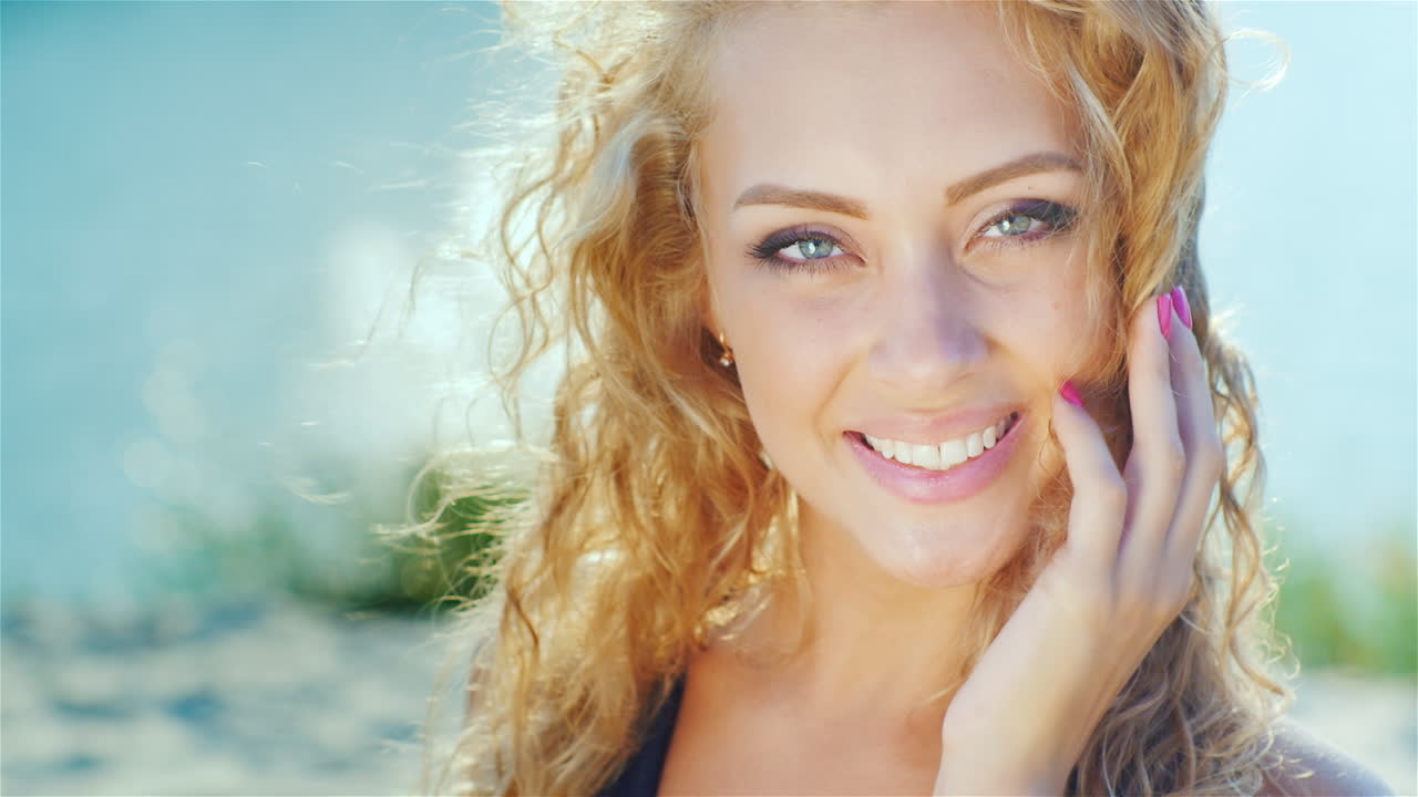 Primo piano di una bella giovane donna che sorride alla telecamera in una giornata di sole in spiaggia, vicino al mare.