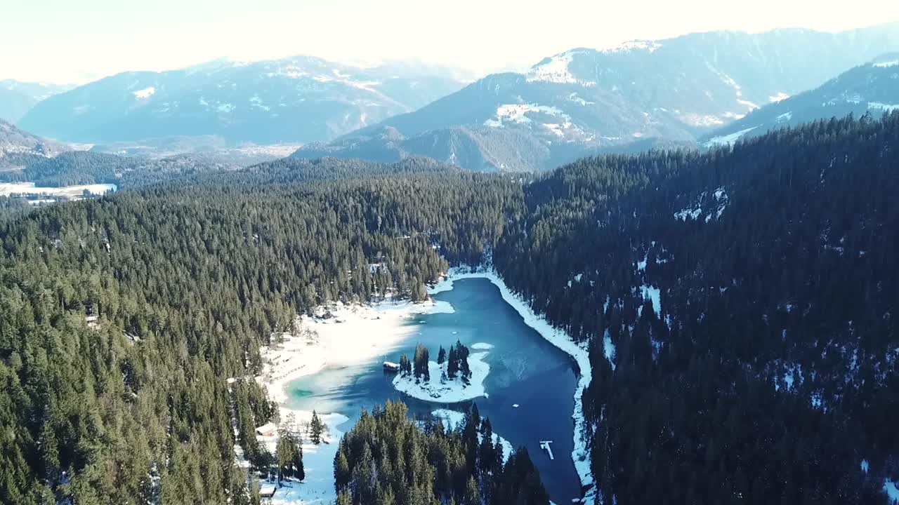 Aerial view of Caumasee, surrounded by snow-dusted trees and mountains, with a clear blue lake in the center