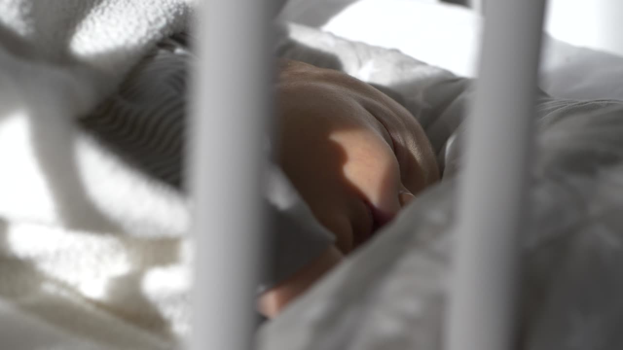 Bebè carino che dorme nella sua culla mentre il sole splende attraverso la finestra, primo piano.