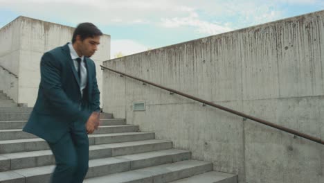 un hombre de negocios alegre y feliz en un traje está bailando activamente mientras baja las escaleras. escena rodada en un parque de hormigón urbano al lado del centro de negocios. día soleado.