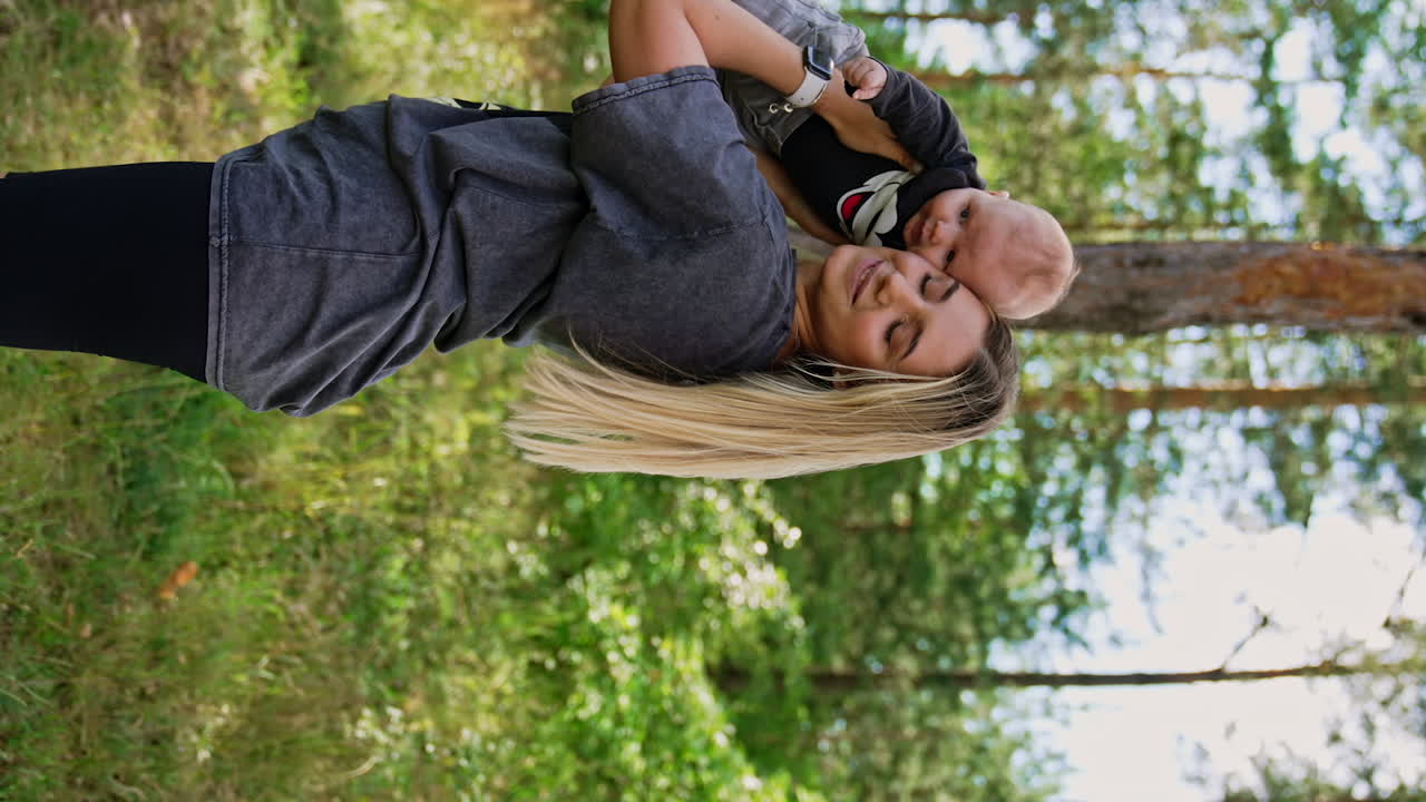 Beautiful blonde Caucasian woman holding a tiny baby boy. Mother lifting her child over the head and presses adorable kid to her cheek. Vertical screen.