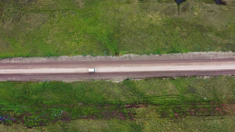 Travel-Car-or-van-driving-on-a-dirt-road-through-Alaska-wild-terrains---aerial-top-down-following-view