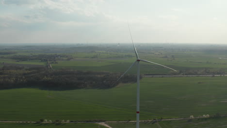 Wind-turbine-towering-high-above-spring-countryside.-Hazy-view-of-landscape-in-windless-weather.-Green-energy,-ecology-and-carbon-footprint-reduction-concept