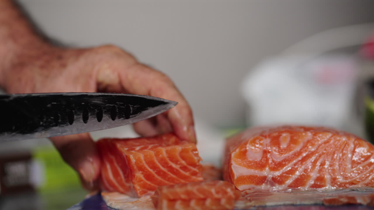 Hands carefully slice fresh salmon into thin pieces with a large knife, perfect for sushi preparation