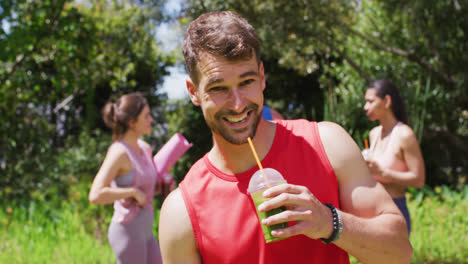 smiling caucasian man with health drink, and diverse group talking after yoga in sunny park