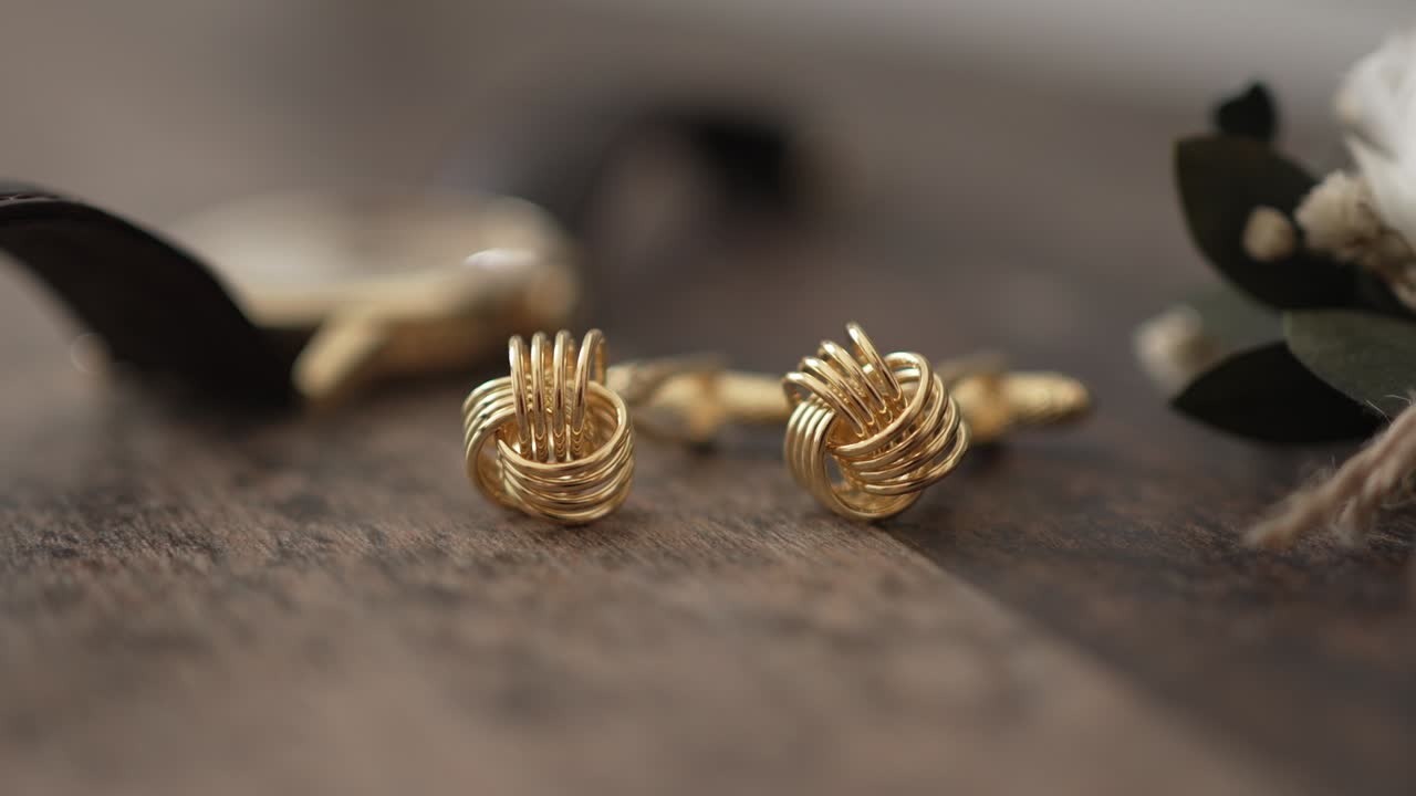 Close up of gold cufflinks with knot design displayed on rustic wooden table