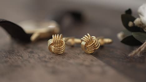 close up of gold cufflinks with knot design displayed on rustic wooden table