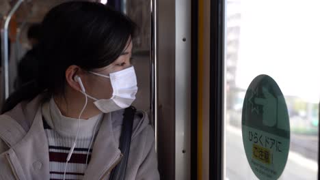 asian girl wearing facemask during corona crisis listening to music on train