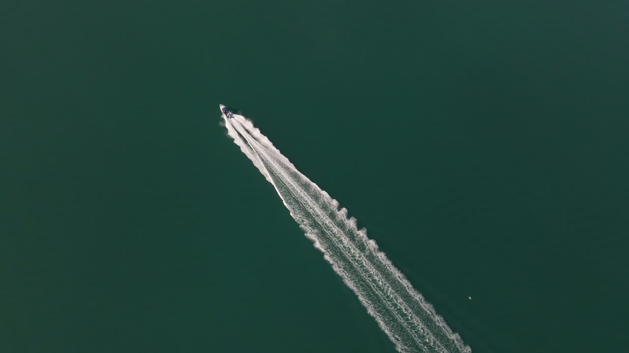 Aerial top-down tracking shot of a speed boat riding straight over turquoise green ocean water