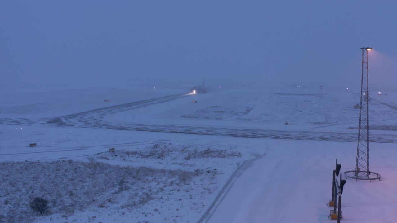Distant airplane taxiing on taxiway in dramatic winter conditions at airport