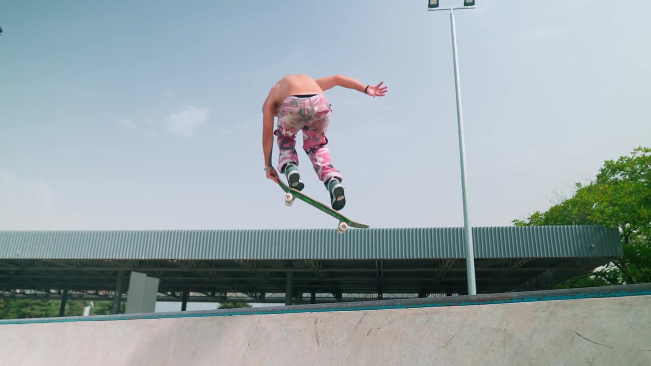Skateboarder a torso nudo salta da una rampa al rallentatore.