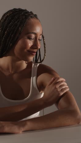 studio skincare beauty shot of young woman with long braided hair putting moisturiser onto arm and shoulder