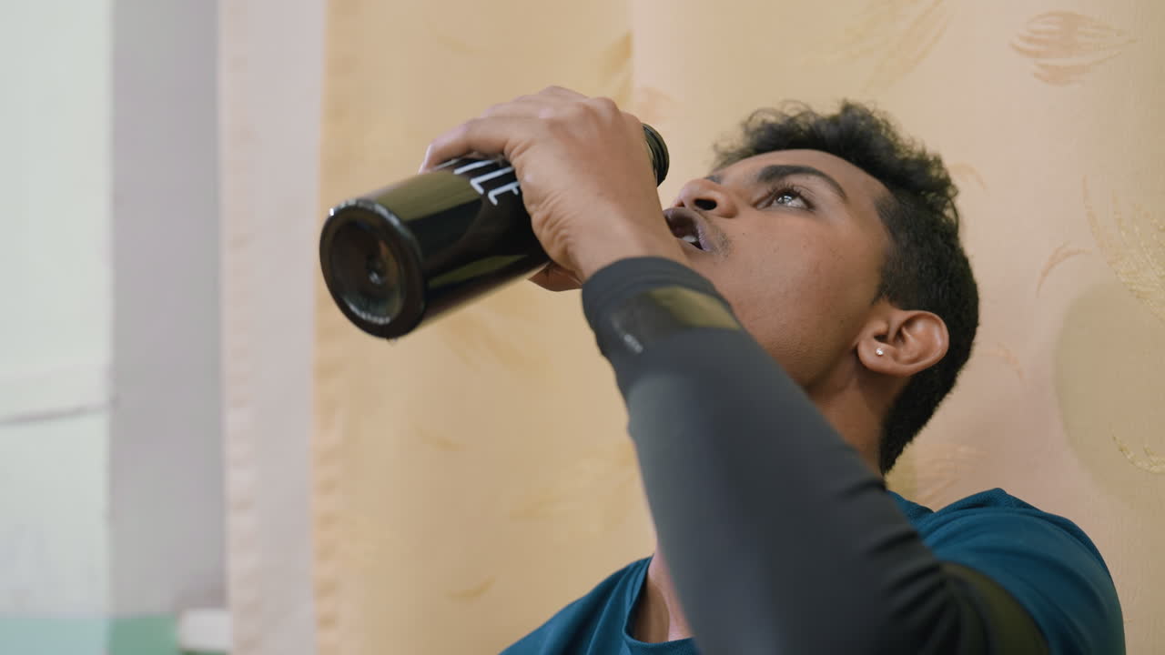 Close up of athlete drinking water from bottle after training session, highlighting hydration, refreshment, and recovery process, showing discipline