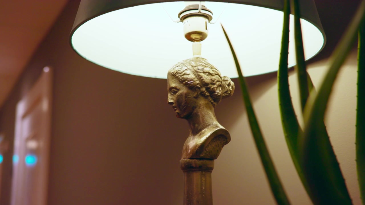 Lampada da tavolo con busto dorato e paralume bianco che emana una luce calda e soffusa. L'elegante design di ispirazione romana aggiunge un fascino senza tempo; i dettagli intricati della statua contrastano splendidamente con il paralume moderno.