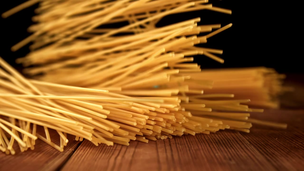 Spaghetti secchi che cadono su un tavolo di legno al rallentatore