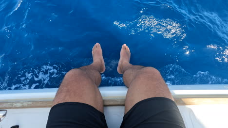 a man sits on the side of a moving boat as the ocean passes underneath