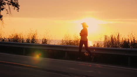 silhouette of a woman who runs along the road along the sea at sunset active middle aged people