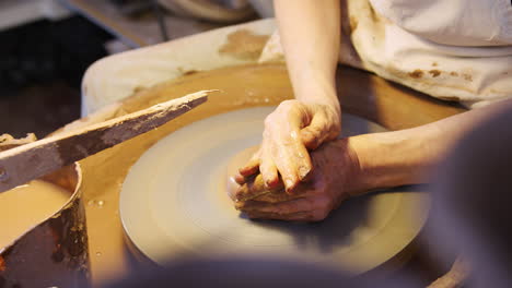 close up of male potter shaping clay for pot on pottery wheel in ceramics studio