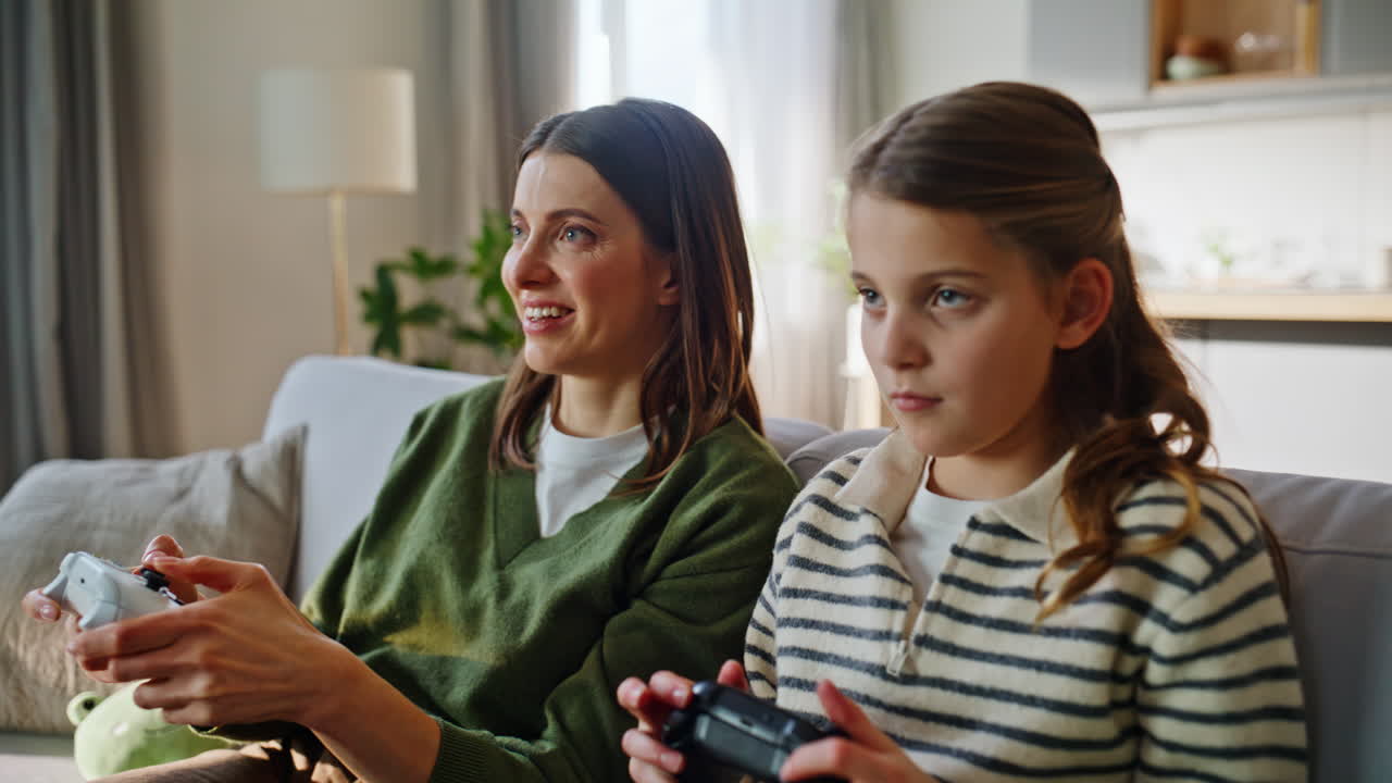 Primo piano: mani di sorelle che premono i joystick giocando a un videogioco sul divano. Famiglia turbata.