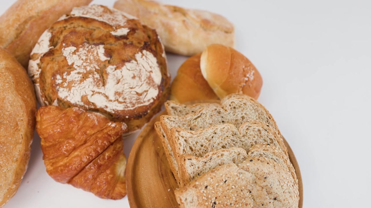 Sakte kamerarotasjon rundt surdeigsbrød, croissanter og skivet fullkornsbrød på hvit overflate