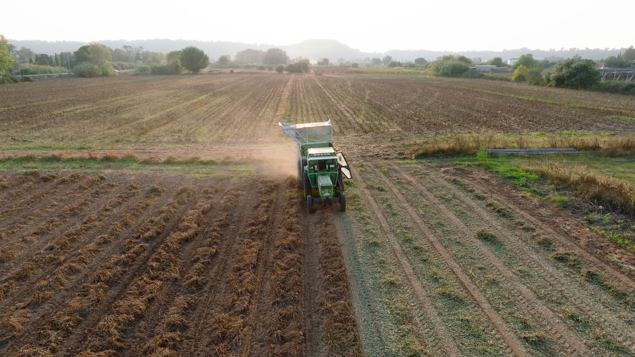 aéreo: volando hacia atrás delante de un tractor arando el suelo durante la puesta del sol