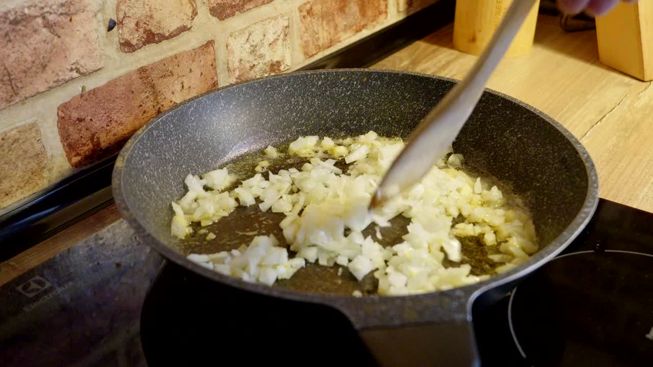 Caramelized onions in olive oil in a pan, chef stirring the dish while preparing breakfast
