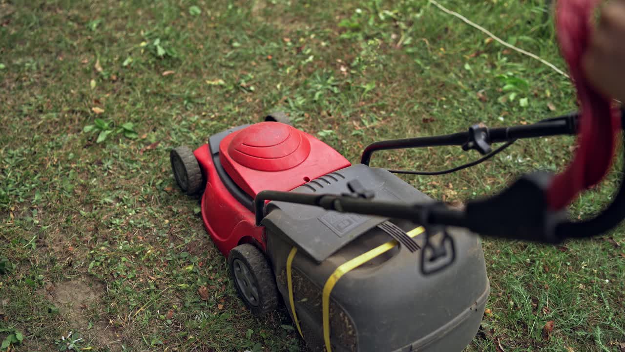 Lawn mower cutting the grass outdoors. Top view of electric lawn mower on the ground. Worker trimming grass by mowing machine. Gardening activity.