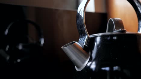 fixed shot of black household domestic kitchen kettle slowly boils for cup of tea coffee with steam water vapor coming out of metal spout