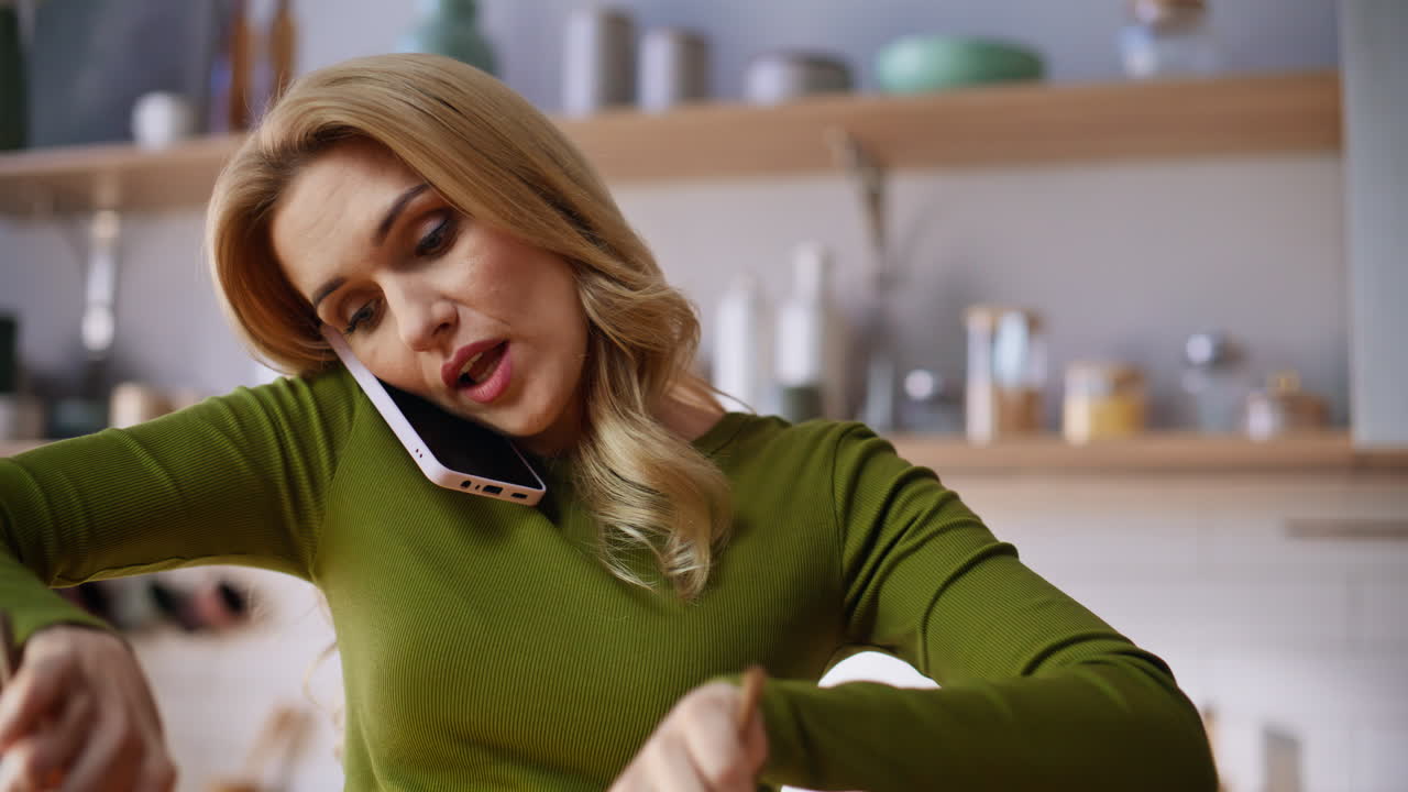Primo piano: donna che mescola un'insalata fresca con cucchiai parlando allo smartphone in una cucina moderna.