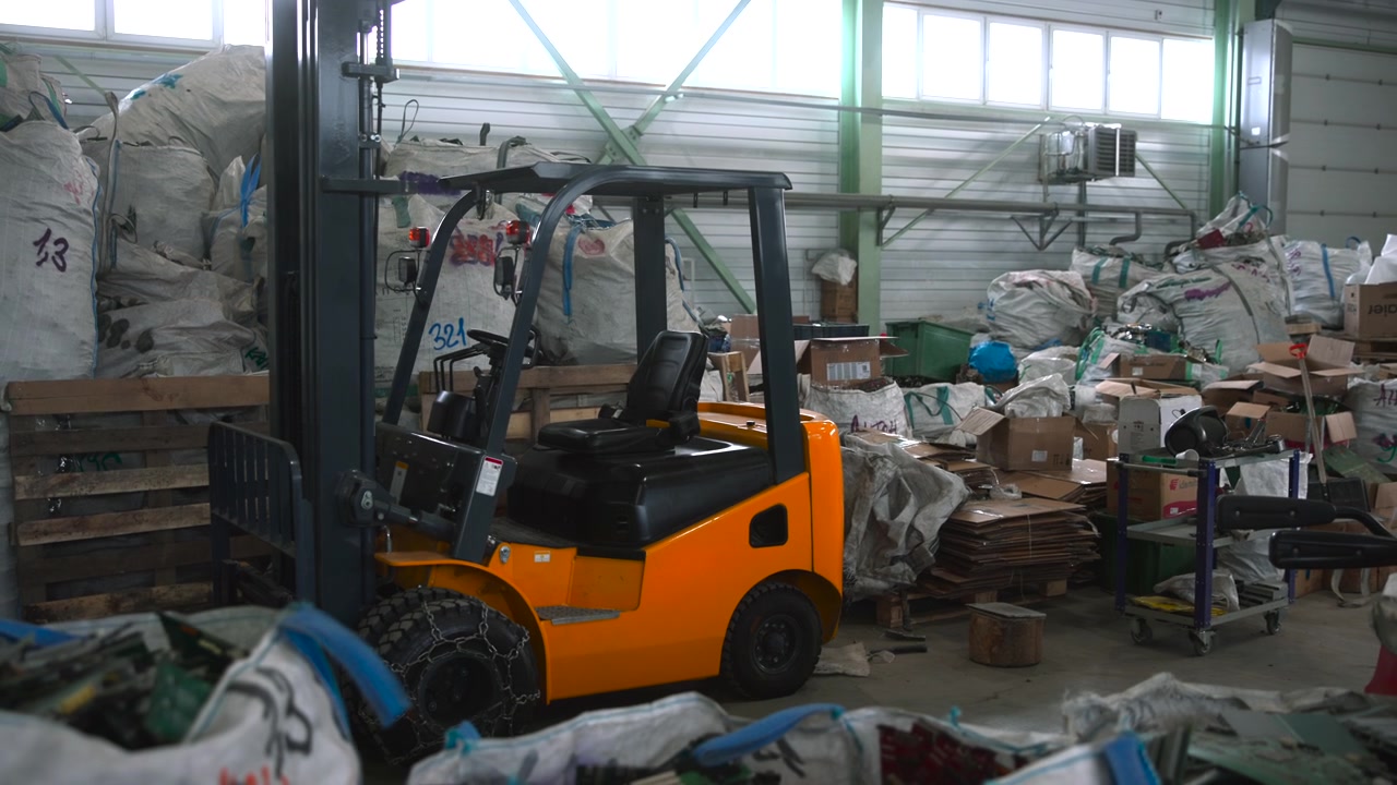 Orange Forklift Parked Inside Cluttered Warehouse Surrounded By Sacks, Pallets, Cardboard Boxes And Scattered