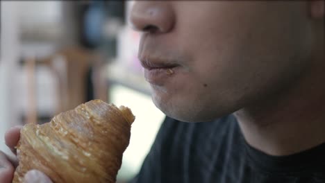 close up view to an asian man while grab and eat fresh french croissant