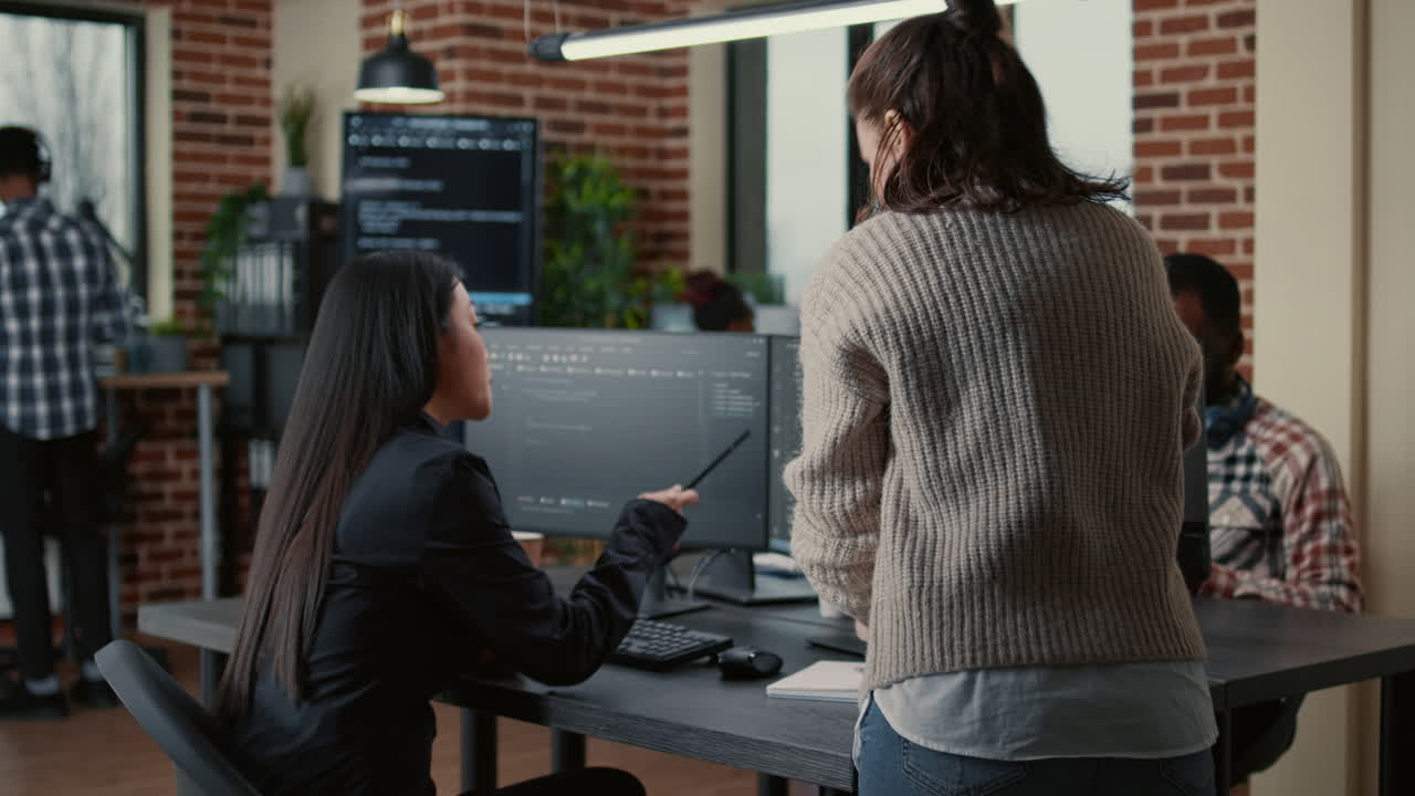 Programer pointing pencil at computer screen with software compiling code explaining source algorithm to coworker