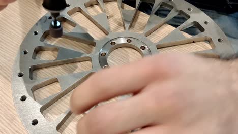 close up of hands of middle aged man sanding down a cut off piece of a metal or steel bar which is on the wooden table surface